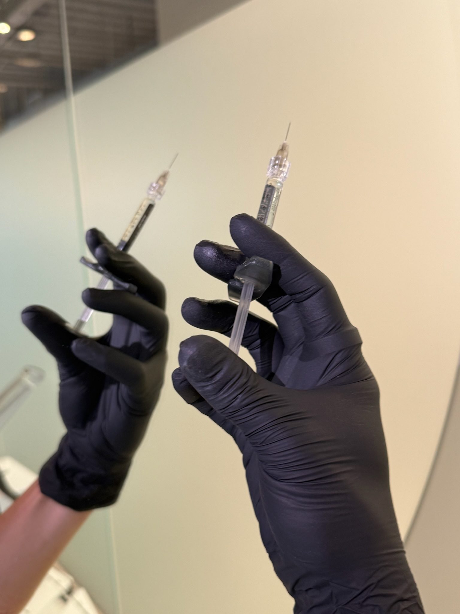 Two gloved hands holding syringes with clear liquid.
