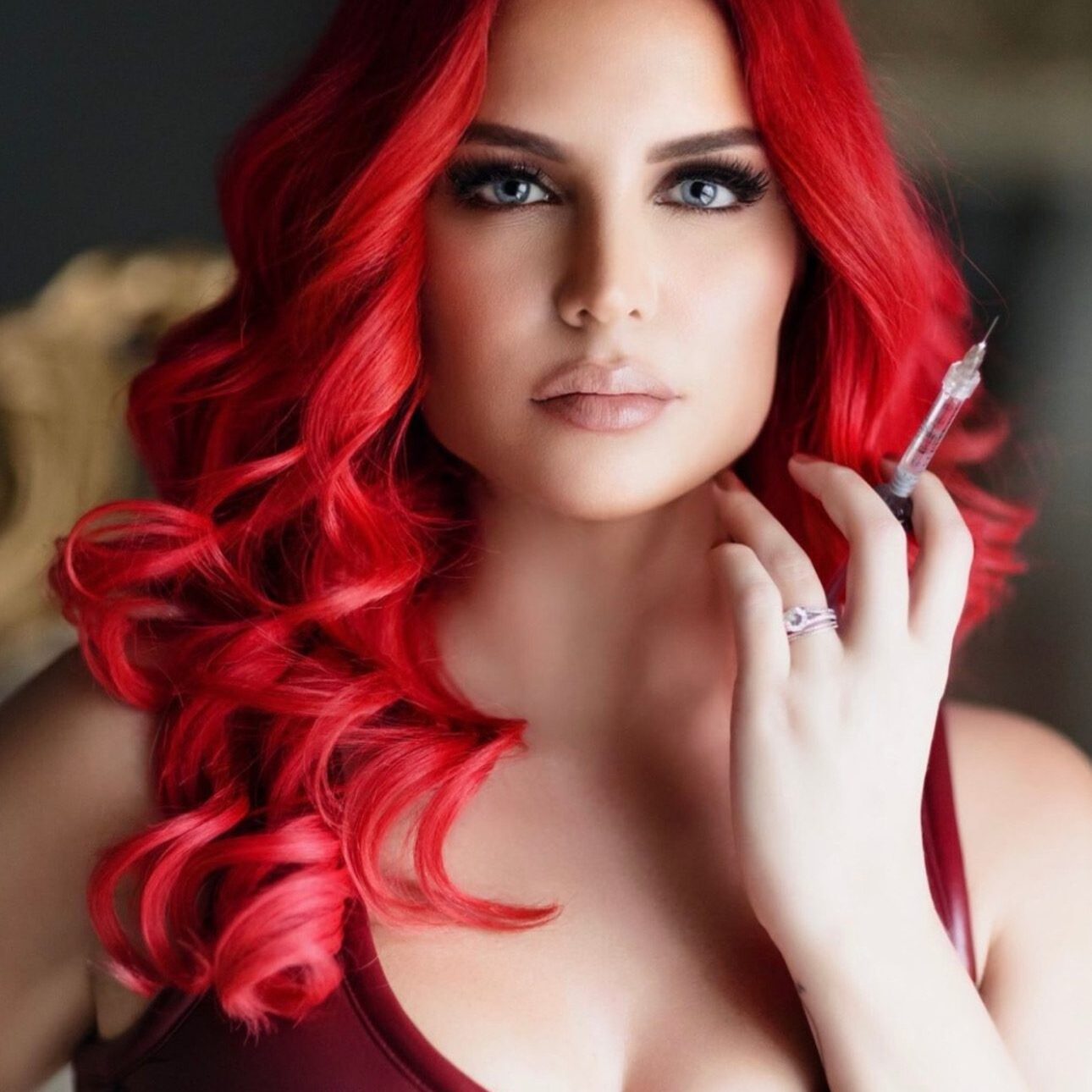 Woman with vibrant red hair and striking makeup poses elegantly.